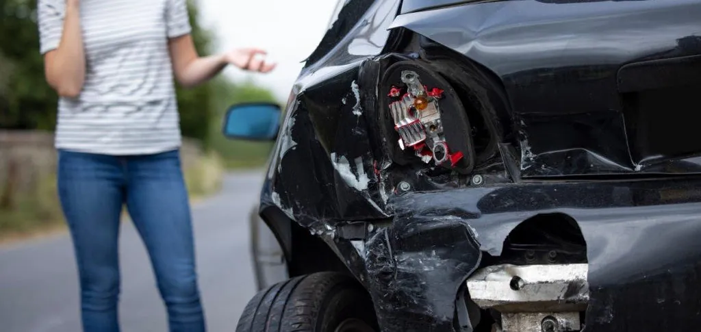 Woman on phone gesturing near damaged black car, illustrating aftermath of car accident and importance of legal guidance in personal injury cases.